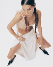 Model in cream top and white skirt with a long braid posing against a white background by Umur Ozcan