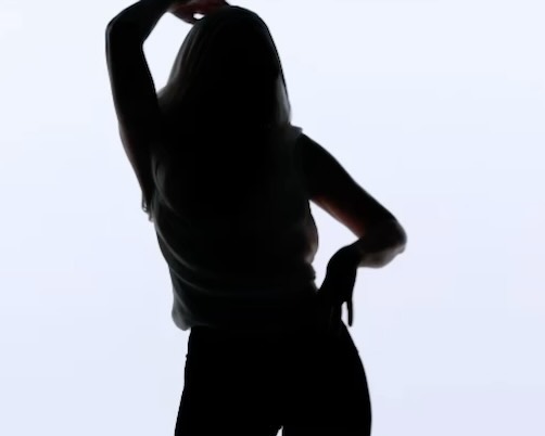 Silhouette of adult female with arm raised and hand on hip against a solid bright background, showing contrast and body shape.