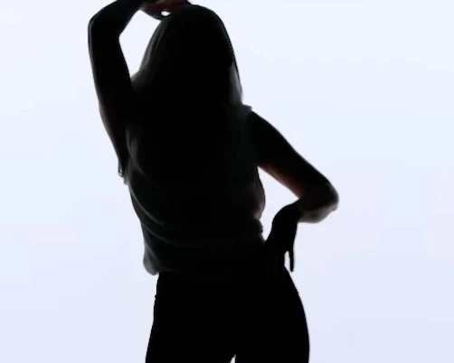 Silhouette of adult female with arm raised and hand on hip against a solid bright background, showing contrast and body shape.