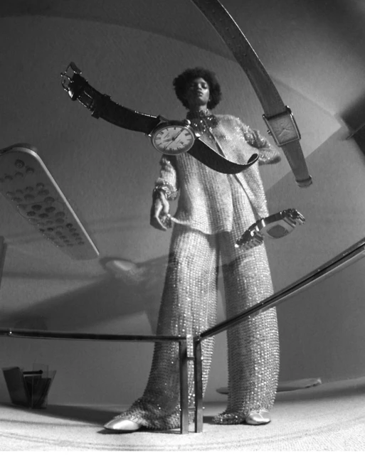 Fashion shot in black and white, with a woman in sparkling clothing surrounded by floating wristwatches in an indoor setting.