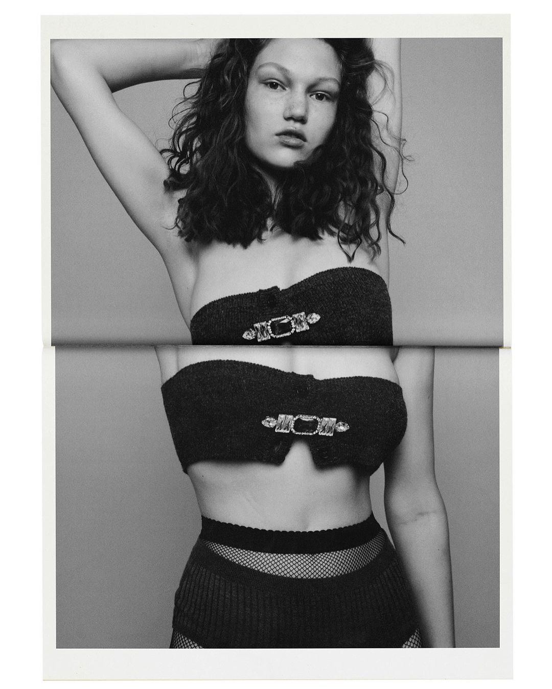 Monochrome fashion shot of a young female model wearing a two-piece outfit with jewel-like embellishments posing in a photo studio.