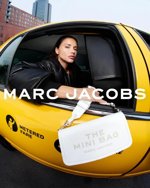 Fashion ad: woman in taxi window, white Marc Jacobs purse on taxi. New York City buildings in distance. Bright yellow cab exterior.