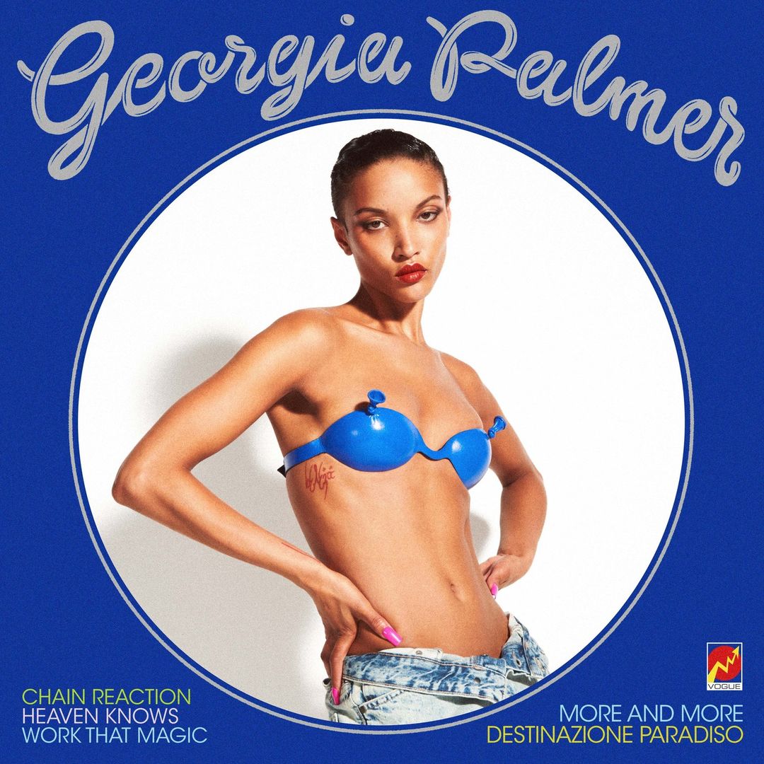 Georgia Palmer poses in a blue bikini bra and denim shorts against a white studio background, framed by a blue circle border and stylized text.