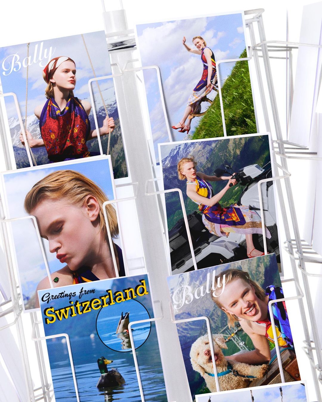 Rack of postcards features a model in a fashion photoshoot backdrop featuring Switzerland's mountains and lakes, plus a dog.