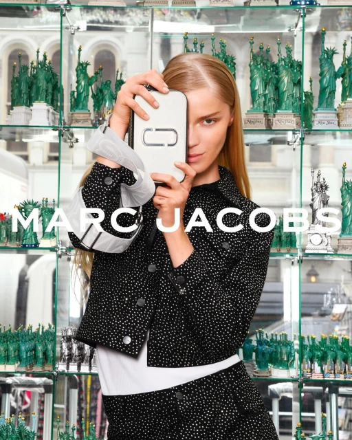 Fashion shot featuring a blonde adult woman holding a Marc Jacobs branded white phone case, wearing a sparkling black jacket and skirt.