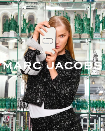 Fashion shot featuring a blonde adult woman holding a Marc Jacobs branded white phone case, wearing a sparkling black jacket and skirt.