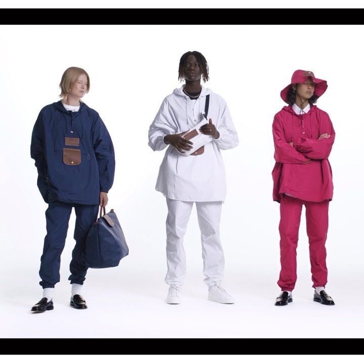 Three fashion models stand in a studio wearing matching athleisure outfits in blue, white and pink, holding bags and accessories.