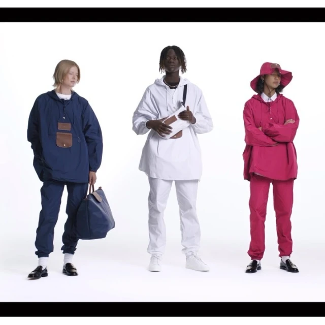 Three fashion models stand in a studio wearing matching athleisure outfits in blue, white and pink, holding bags and accessories.
