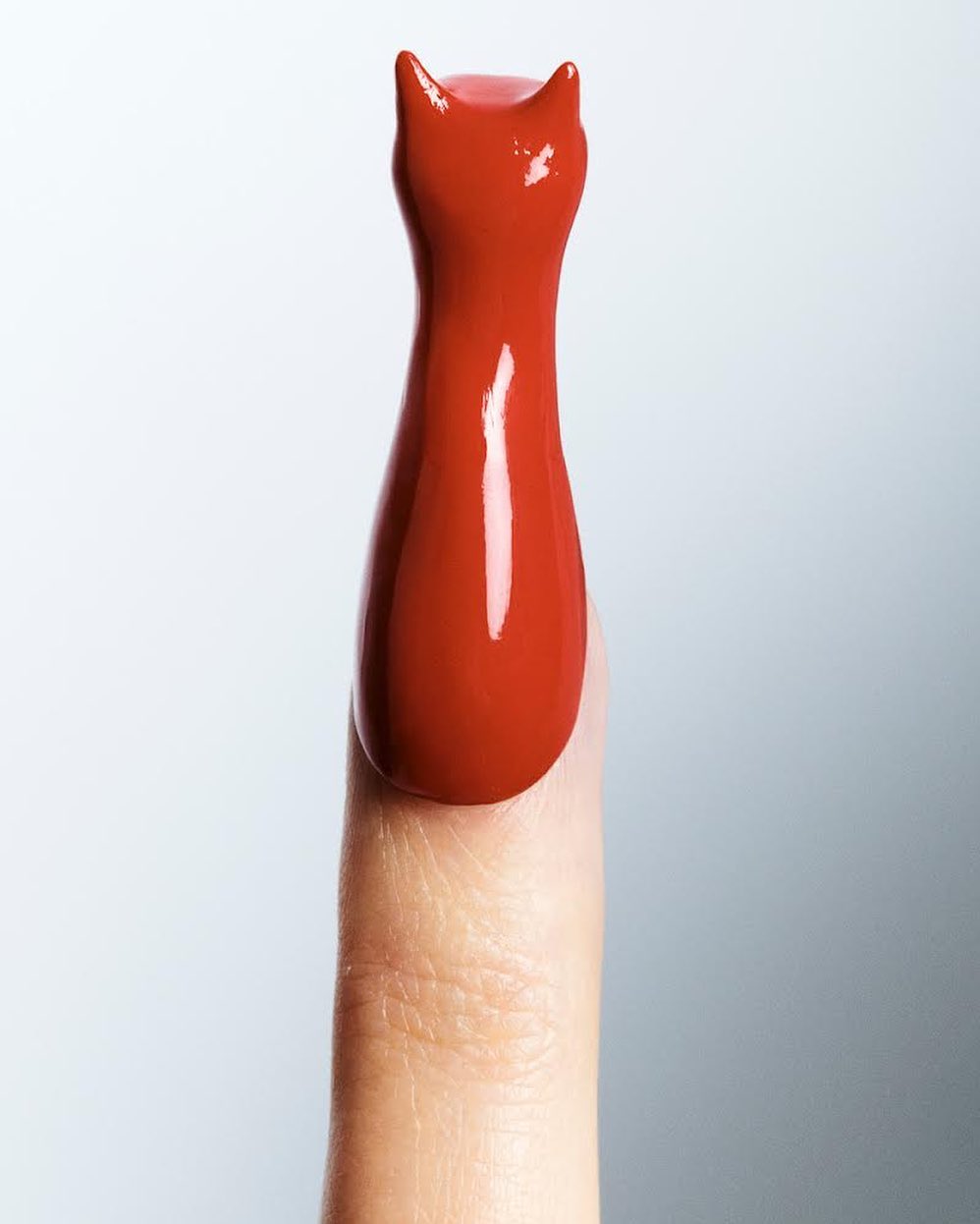 Close-up studio shot of a single adult finger coated in red nail polish, styled into the shape of a cat figure with pointed ears.