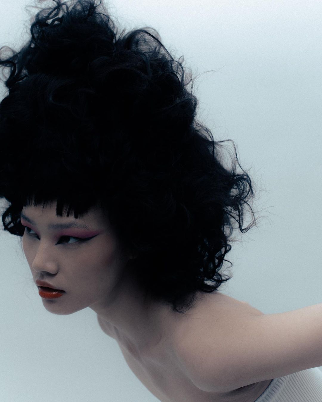 Portrait of a model with voluminous dark curly hair, pink winged eyeliner, and red lipstick by Vanessa Granda