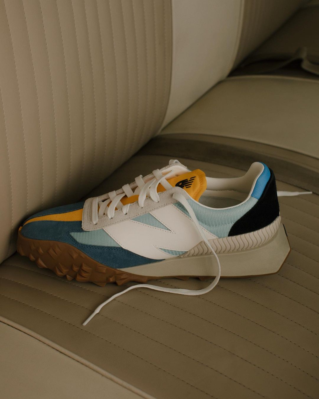 Colorful sneaker with white, blue, yellow, and black panels resting on a vintage car seat.