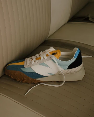 Colorful sneaker with white, blue, yellow, and black panels resting on a vintage car seat.