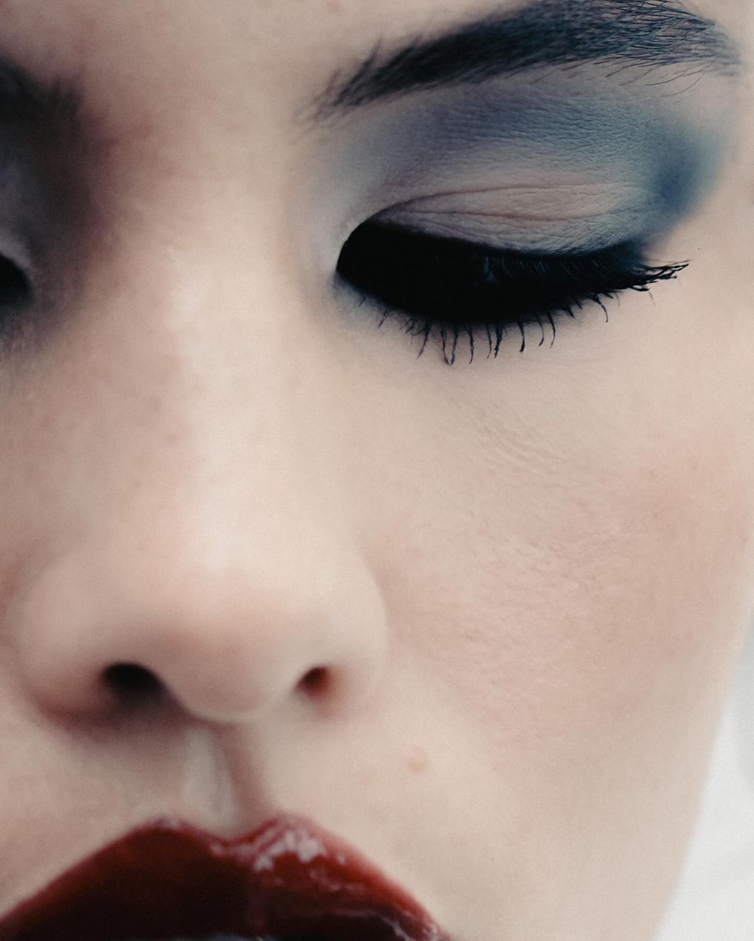 Close-up of a woman's face with dark blue eye makeup and glossy red lipstick, emphasizing beauty and cosmetic details.
