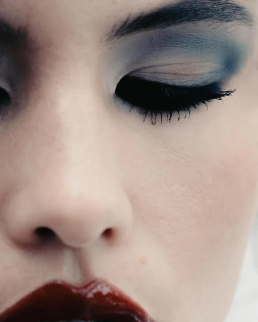 Close-up of a woman's face with dark blue eye makeup and glossy red lipstick, emphasizing beauty and cosmetic details.
