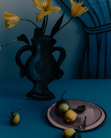 Still life of yellow tulips in a black vase, lemons on a plate and scattered on a blue table against a striped blue curtain.