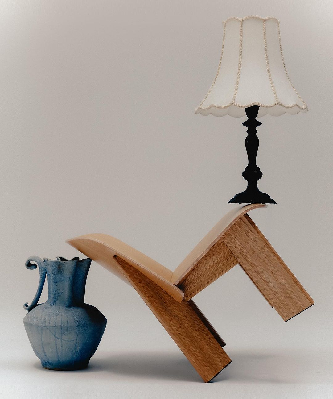 Still life of wooden chair, blue ceramic vase, and white lampshade against a neutral backdrop in a photo studio.