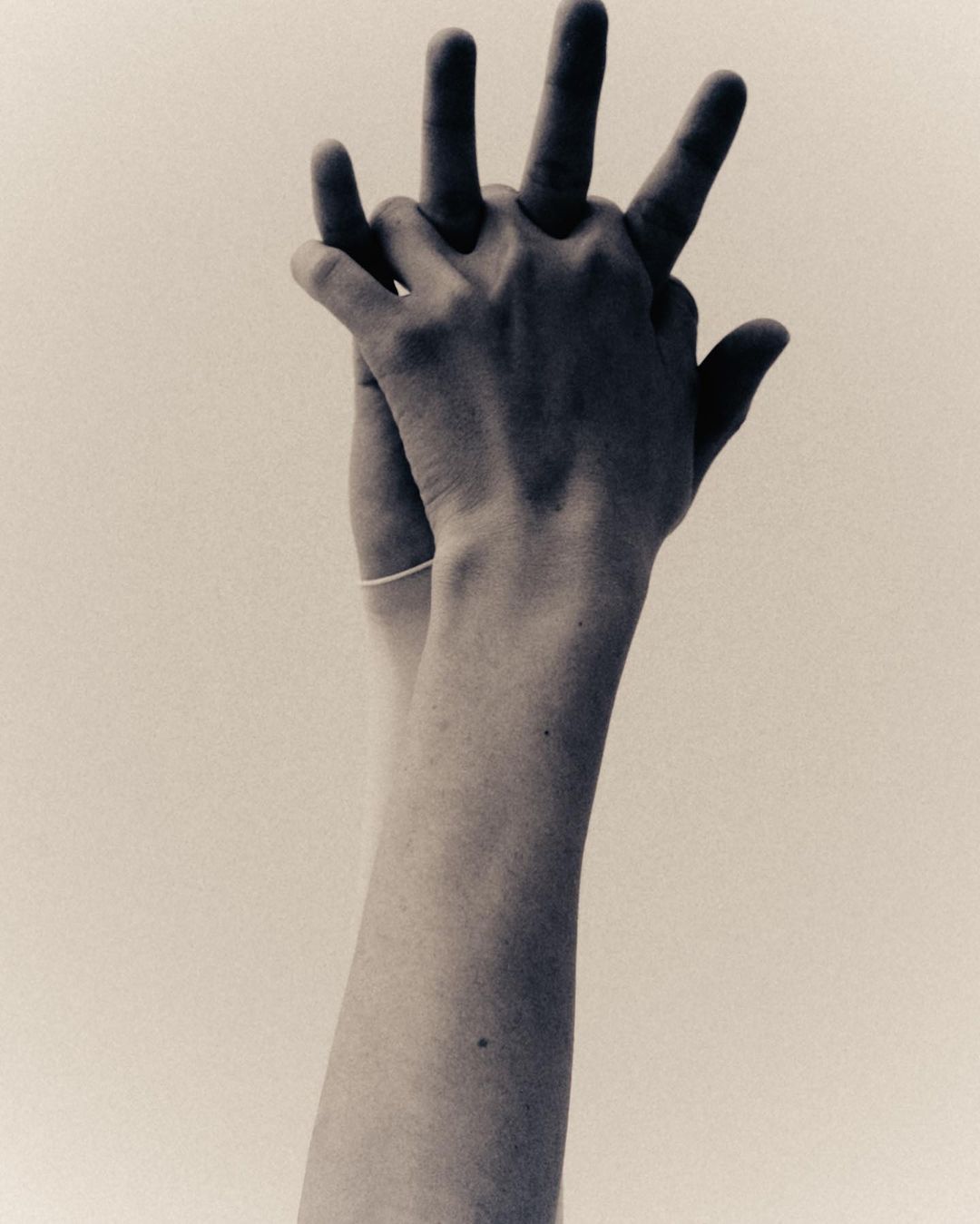 Close-up studio shot of hands interlocking in a black and white style, set against a bright neutral background, emphasizing skin textures.
