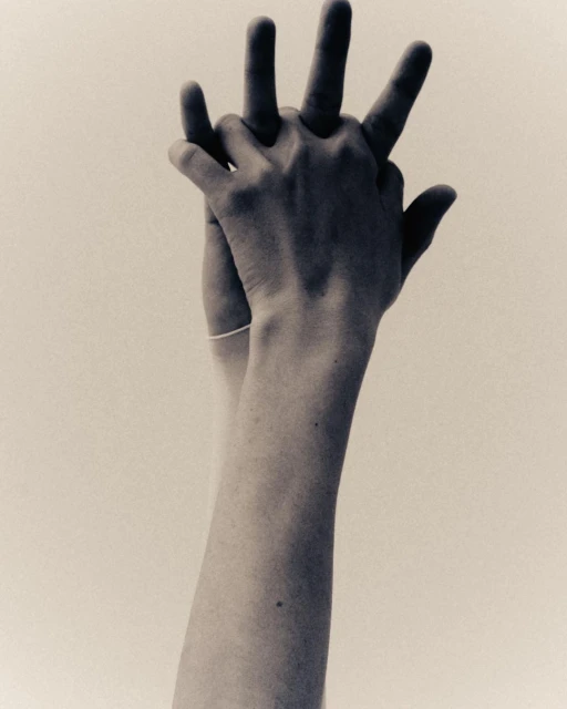 Close-up studio shot of hands interlocking in a black and white style, set against a bright neutral background, emphasizing skin textures.