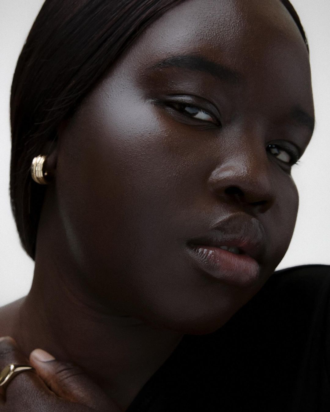 Close-up portrait of a Black woman wearing a small gold hoop earring and a ring, photographed by Vanessa Granda.