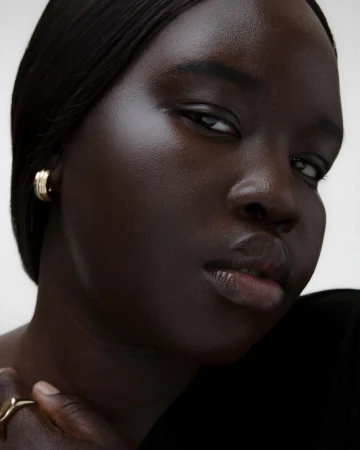 Close-up portrait of a Black woman wearing a small gold hoop earring and a ring, photographed by Vanessa Granda.