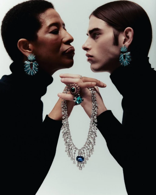 Two people in black turtlenecks display jewellery against a white background. A woman and a younger person hold a diamond necklace.