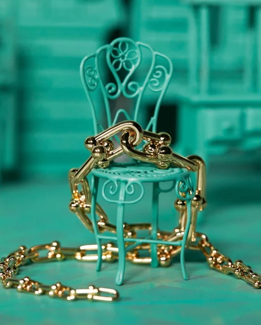 Gold chainlink necklace draped on a miniature ornate aqua chair, macro studio shot on an aqua background.
