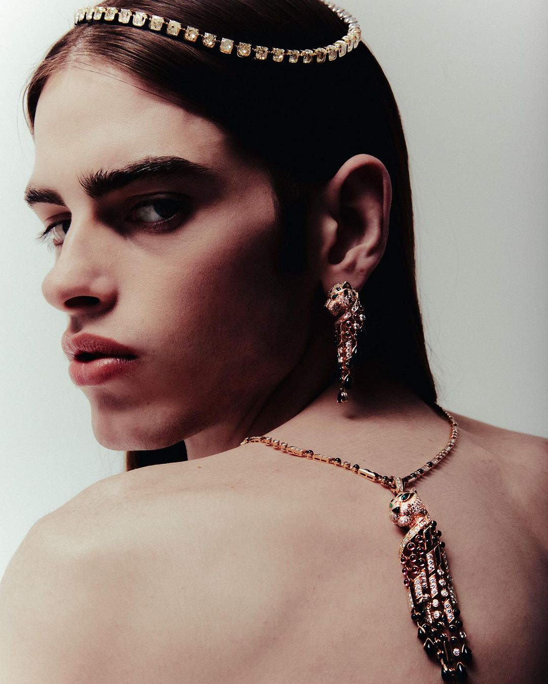 Close-up studio shot of adult male model in gold cat jewelry and diamond headband looking back over shoulder in a beauty fashion editorial.