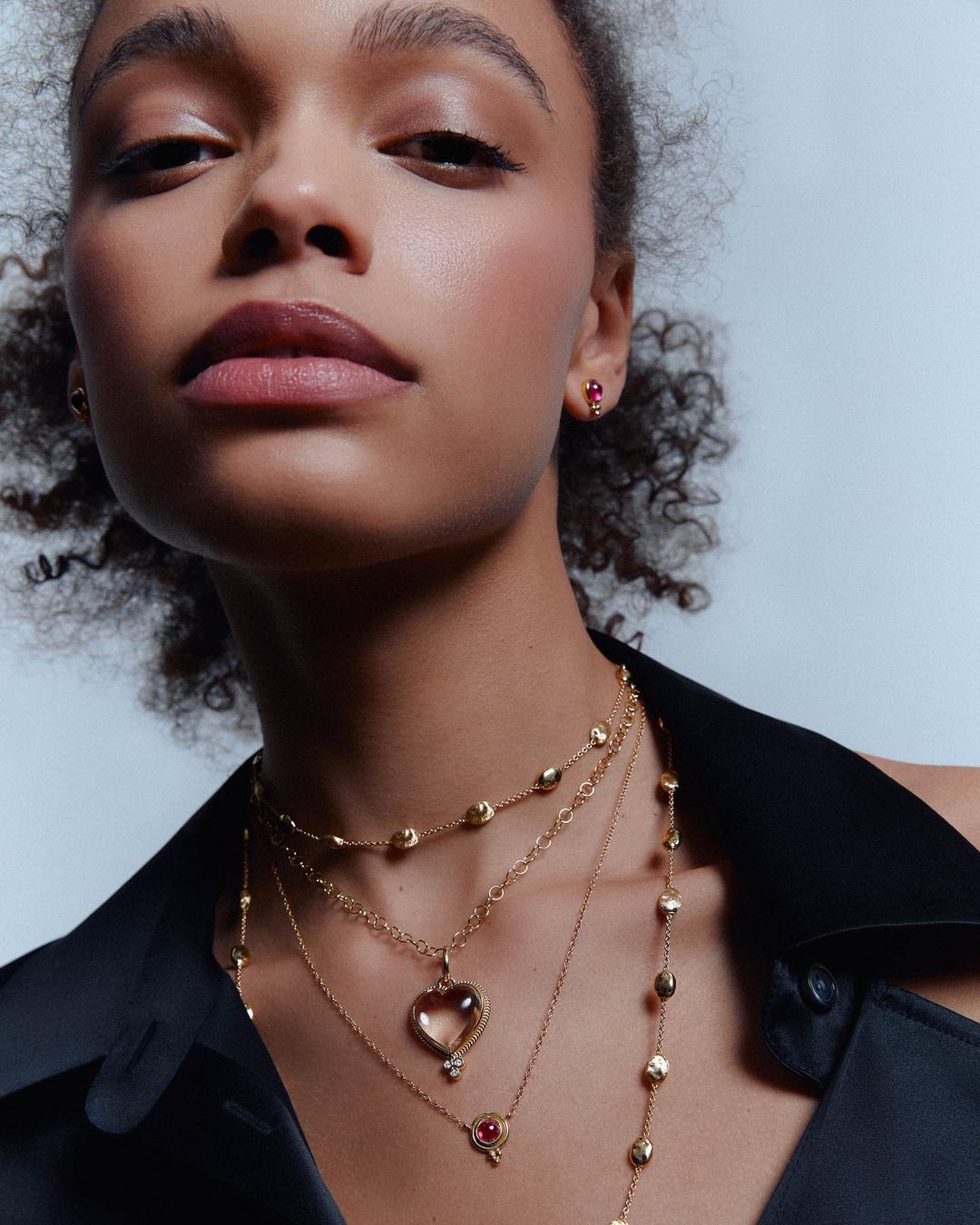 Close-up portrait of a woman wearing gold layered necklaces and small red gemstone earrings by photographer Vanessa Granda