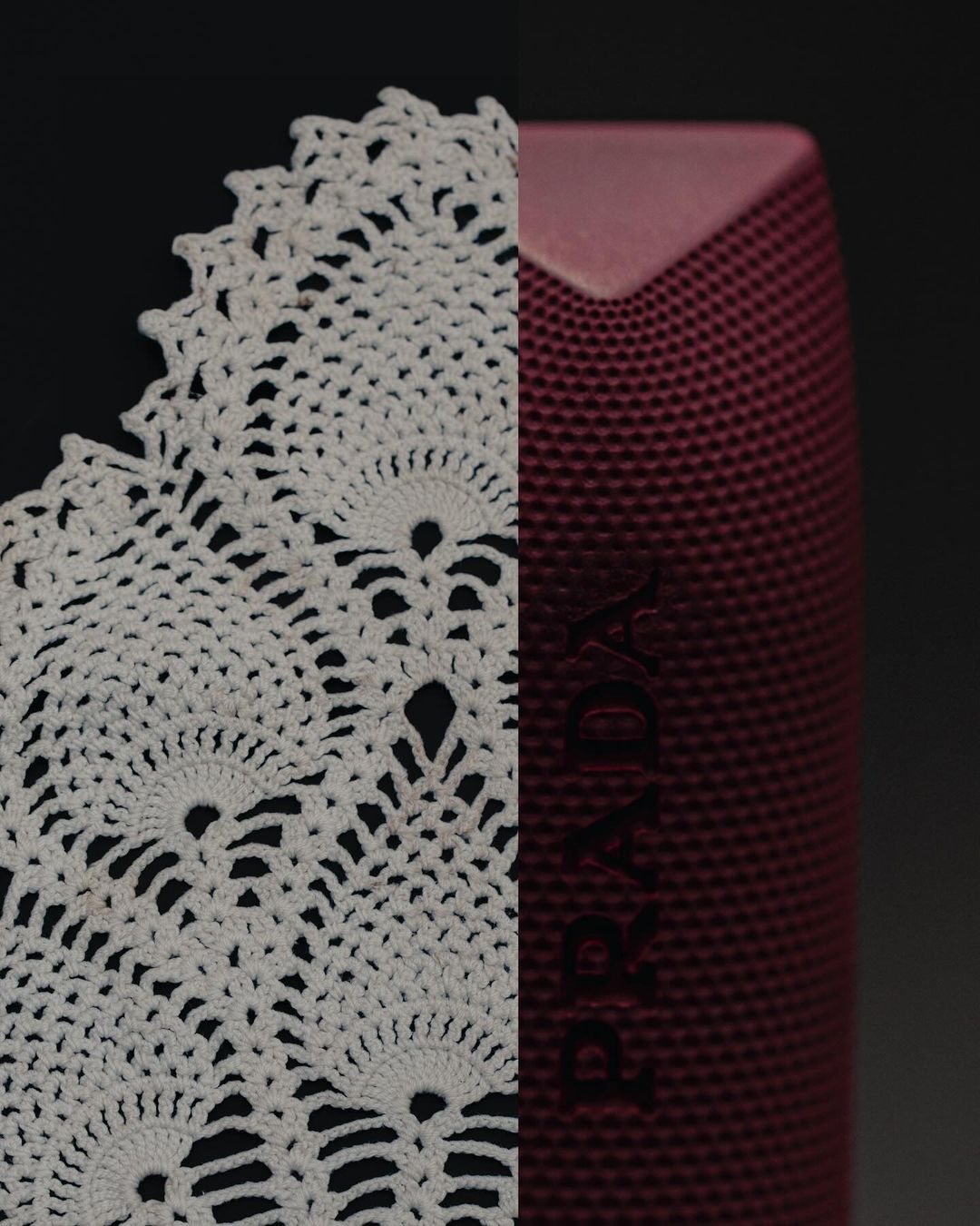 Close-up studio shot features a white crocheted doily and a maroon-colored PRADA speaker against a dark background.