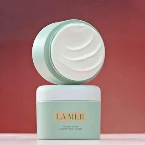 La Mer body cream product shot. The container for the cream is a soft aqua color, with a frosted cream lid stacked on top of it.
