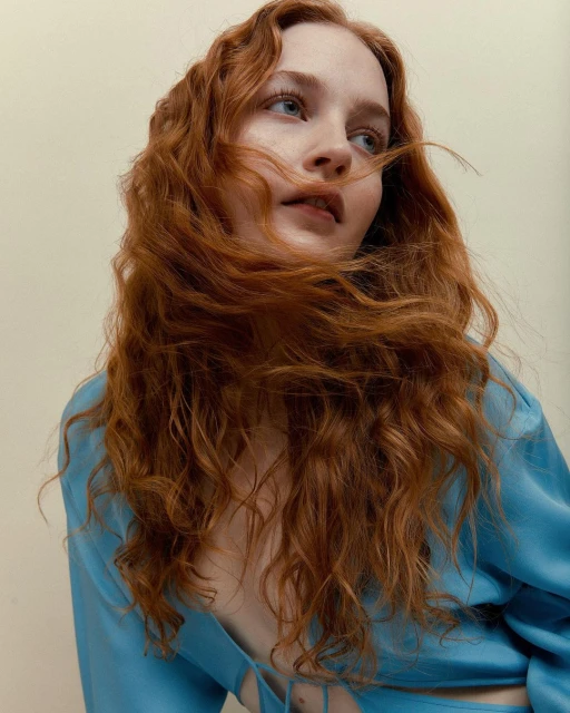 A portrait showcases a woman with flowing, reddish-brown hair against a neutral backdrop, wearing a stylish, light blue top.