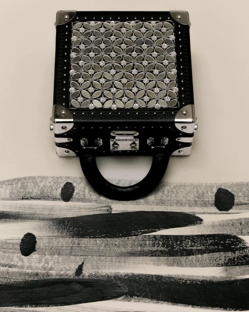 Black handbag featuring a silver floral pattern displayed against a cream background with black brush stroke patterns and silver hardware.