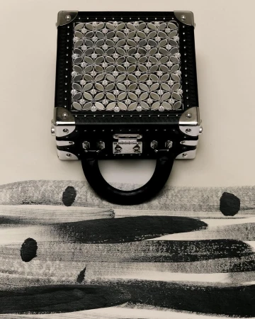 Black handbag featuring a silver floral pattern displayed against a cream background with black brush stroke patterns and silver hardware.