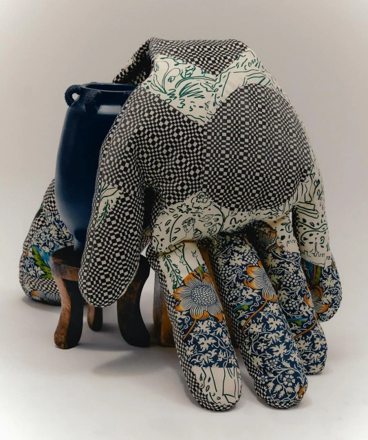 Still life of a blue ceramic vase atop a brown wooden stool, draped with a patterned, quilted textile in a studio setting.