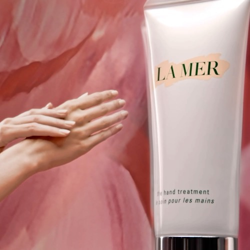 Close-up of hands beside a La Mer hand treatment tube against a painterly pink backdrop, photographed by Vanessa Granda.