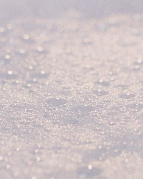 Abstract close-up of glittering white material, possibly snow or a textured surface, with soft bokeh-style lighting.