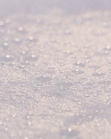 Abstract close-up of glittering white material, possibly snow or a textured surface, with soft bokeh-style lighting.