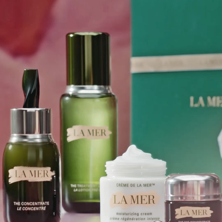 La Mer skincare product line featuring creams, lotions, and concentrates in a studio setting with soft pink and green backgrounds.