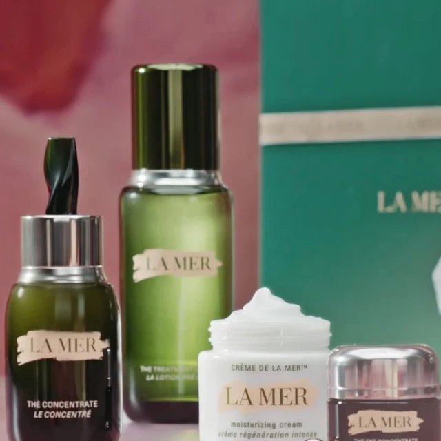 La Mer skincare product line featuring creams, lotions, and concentrates in a studio setting with soft pink and green backgrounds.
