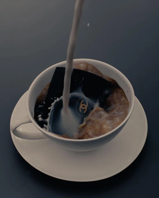 Milk being poured into a white ceramic teacup filled with cereal; a Chanel logo is visible beneath the stream of liquid.