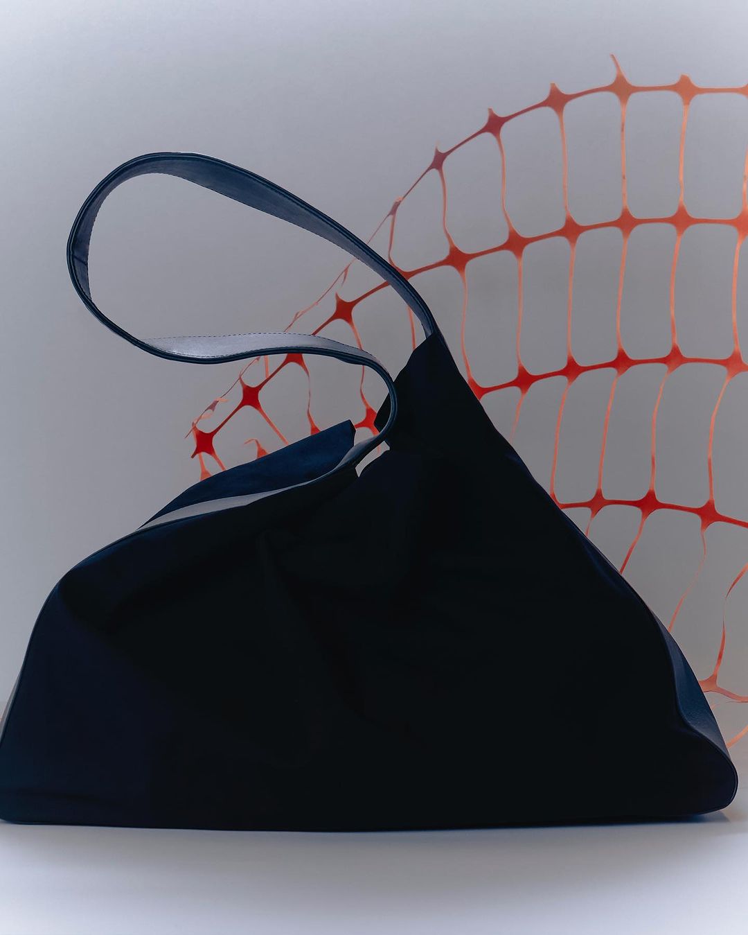 Studio shot of a dark blue tote bag with a blue handle against a white background with a light orange safety fence pattern.