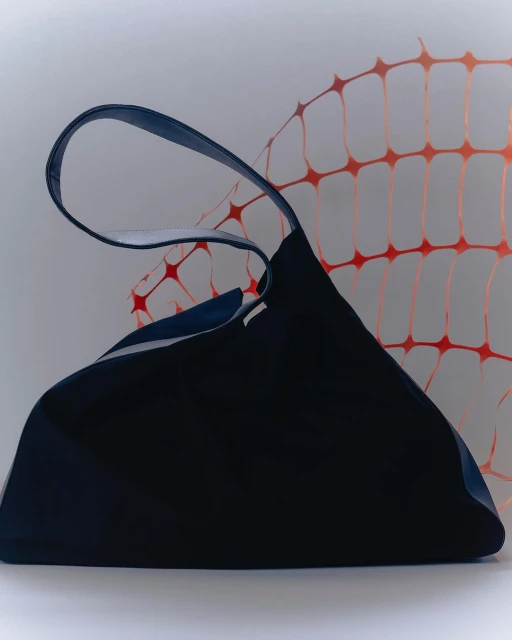Studio shot of a dark blue tote bag with a blue handle against a white background with a light orange safety fence pattern.