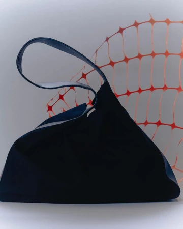 Studio shot of a dark blue tote bag with a blue handle against a white background with a light orange safety fence pattern.