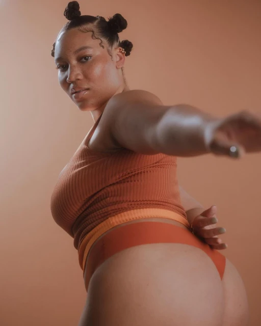 Portrait of a woman in an earth-toned top and bottoms posing against an orange background in a studio setting. Beauty and fashion.