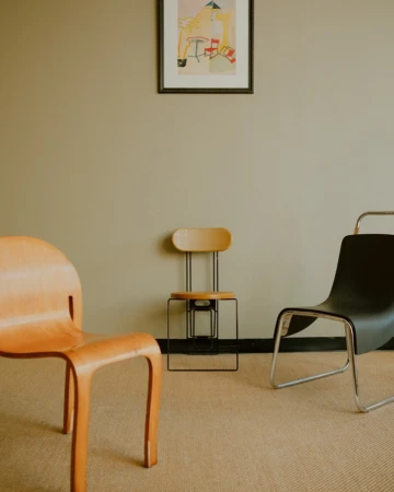 Three distinct chairs arranged in a minimalist room with a framed art print hanging on a plain wall above.