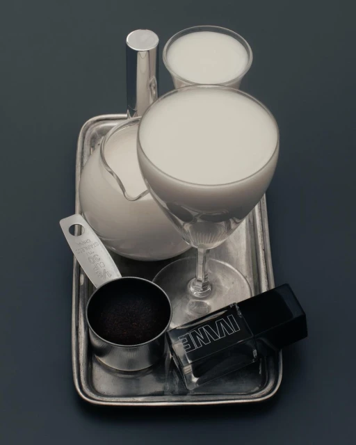 Still life featuring clear drink glasses and a silver tray, along with a measuring cup, black powder, and nail polish bottle.