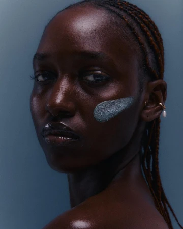 Close-up portrait of a Black woman with braided hair and a green clay mask streak on her cheek by photographer Vanessa Granda