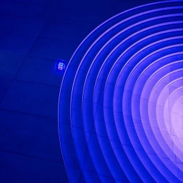 CGI artwork by Vasava featuring concentric circular steps illuminated in vibrant blue and purple light with a small glowing cube on the floor.