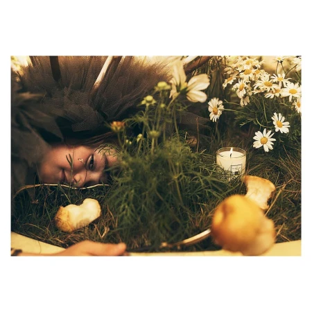 Close-up of a young woman lying in grass surrounded by daisies and a lit candle, photographed by Simon Eeles.
