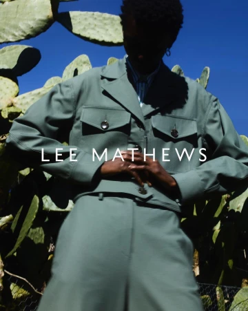 Model in sage green jacket and trousers posing against large cactus plants under a bright blue sky, photographed by Simon Eeles.